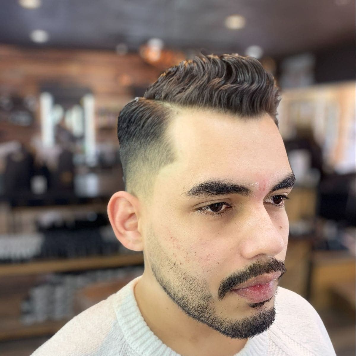 Low fade with wavy pompadour and lined beard