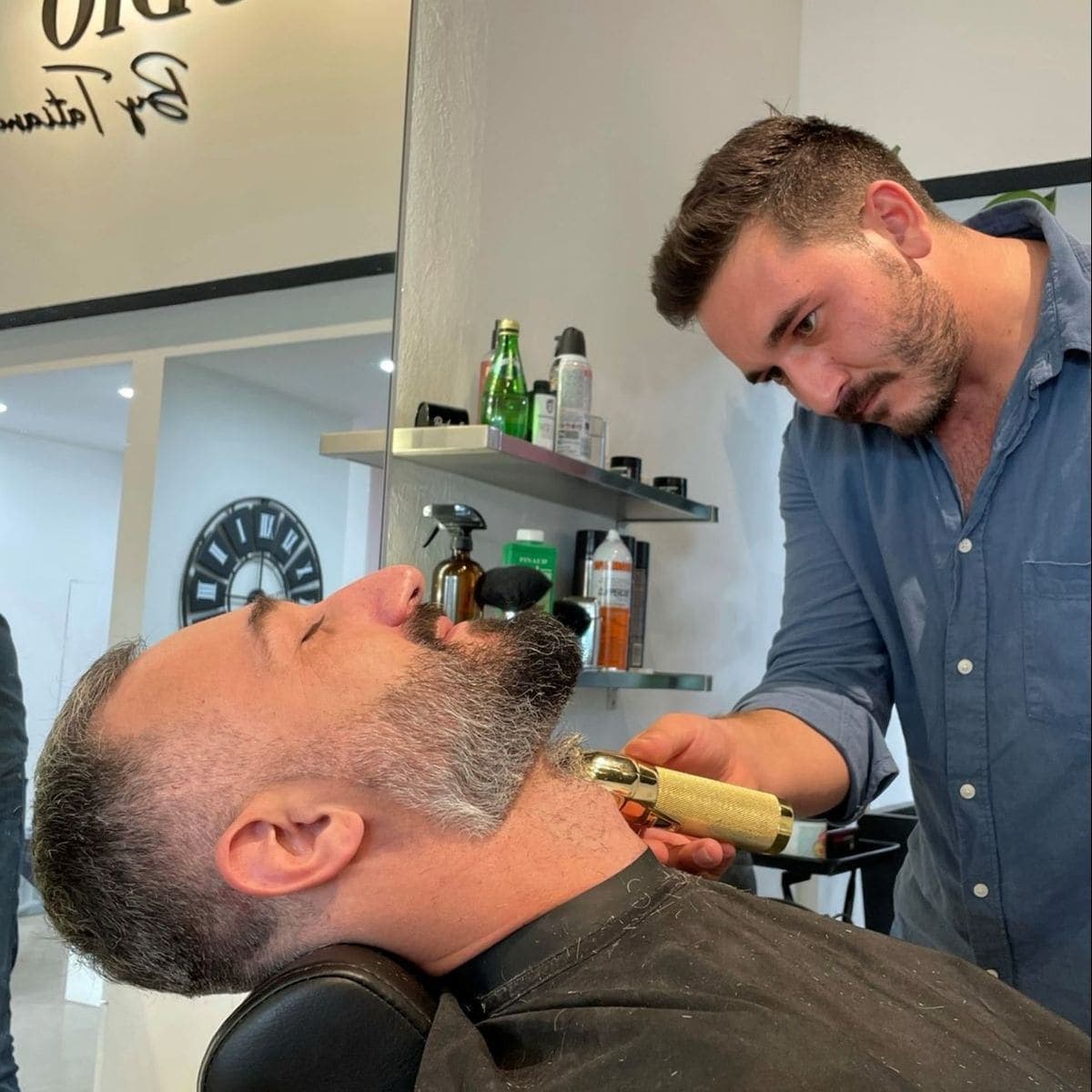 Barber trimming beard with gold clippers
